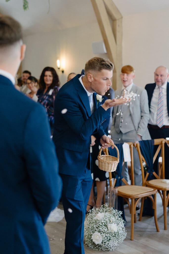 A groomsman holding a basket blows flower petals
