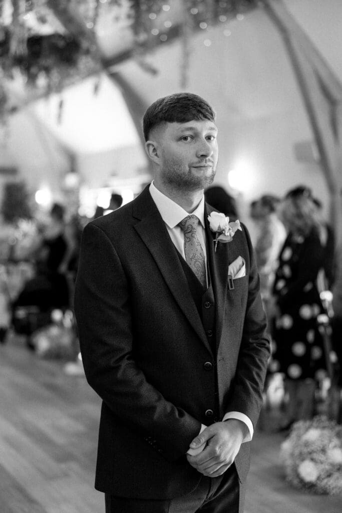 The groom standing at the front of the ceremony room at the River Barn