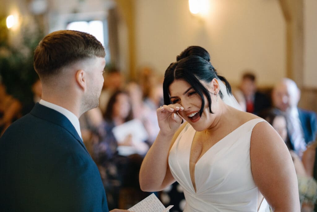 Bride wipes away a tear whilst her groom reads his personalised vows at their River Barn wedding ceremony