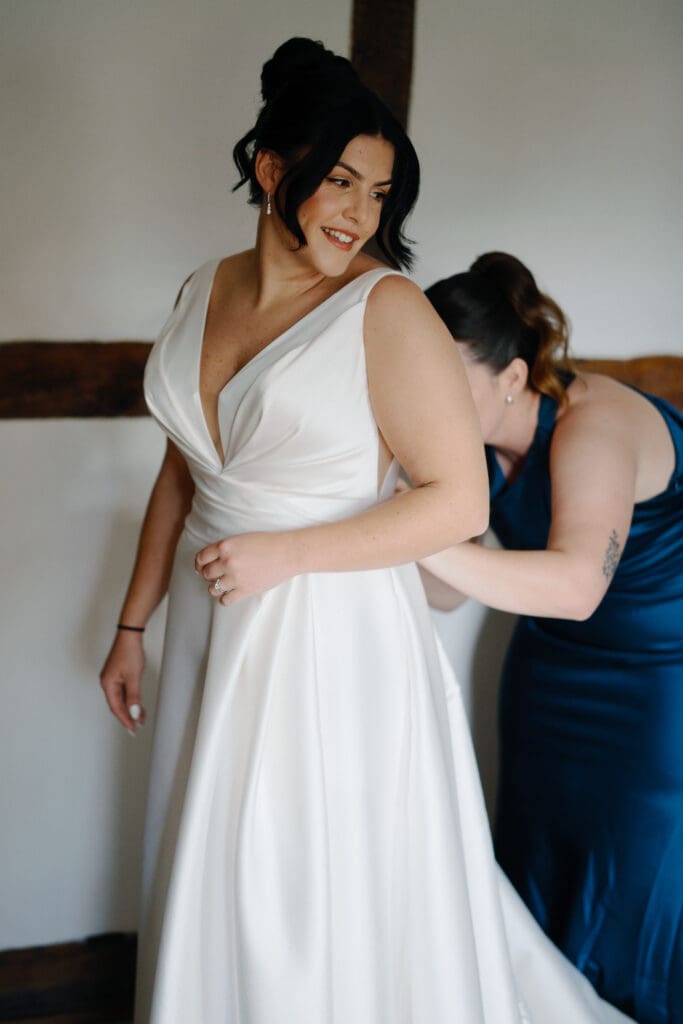 Lucy getting into her wedding dress with the help of her chief bridesmaid, at the River Barn, Lancashire, by Nessworthy Pictures