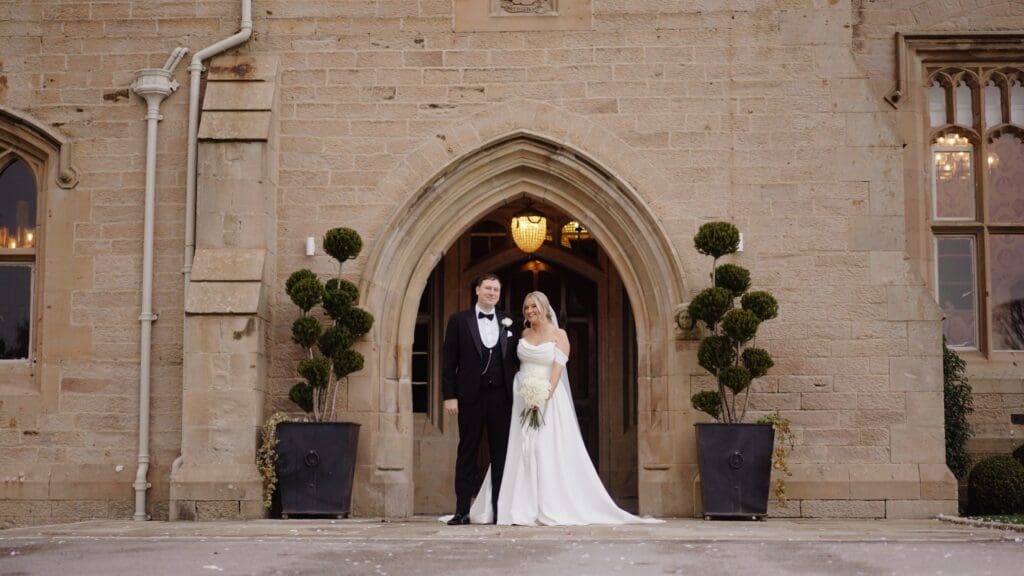 Bride and groom stand together in the doorway of Wennington Hall, Lancaster. A frame from their wedding film, captured by Bill Nessworthy, Lancashire wedding videographer